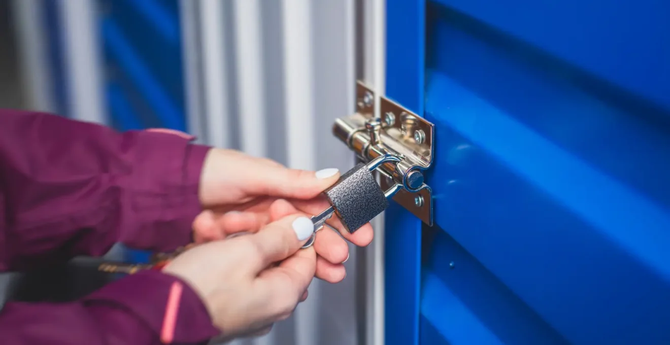 Une main ferme le cadenas d'un box de stockage rempli de cartons.